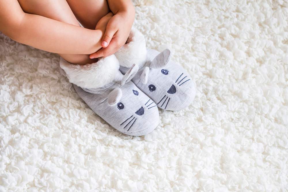 Kinderbeine mit Mauseschuhen sitzend auf einem flauschigen Teppich - Thema Noroviren im Teppichflor